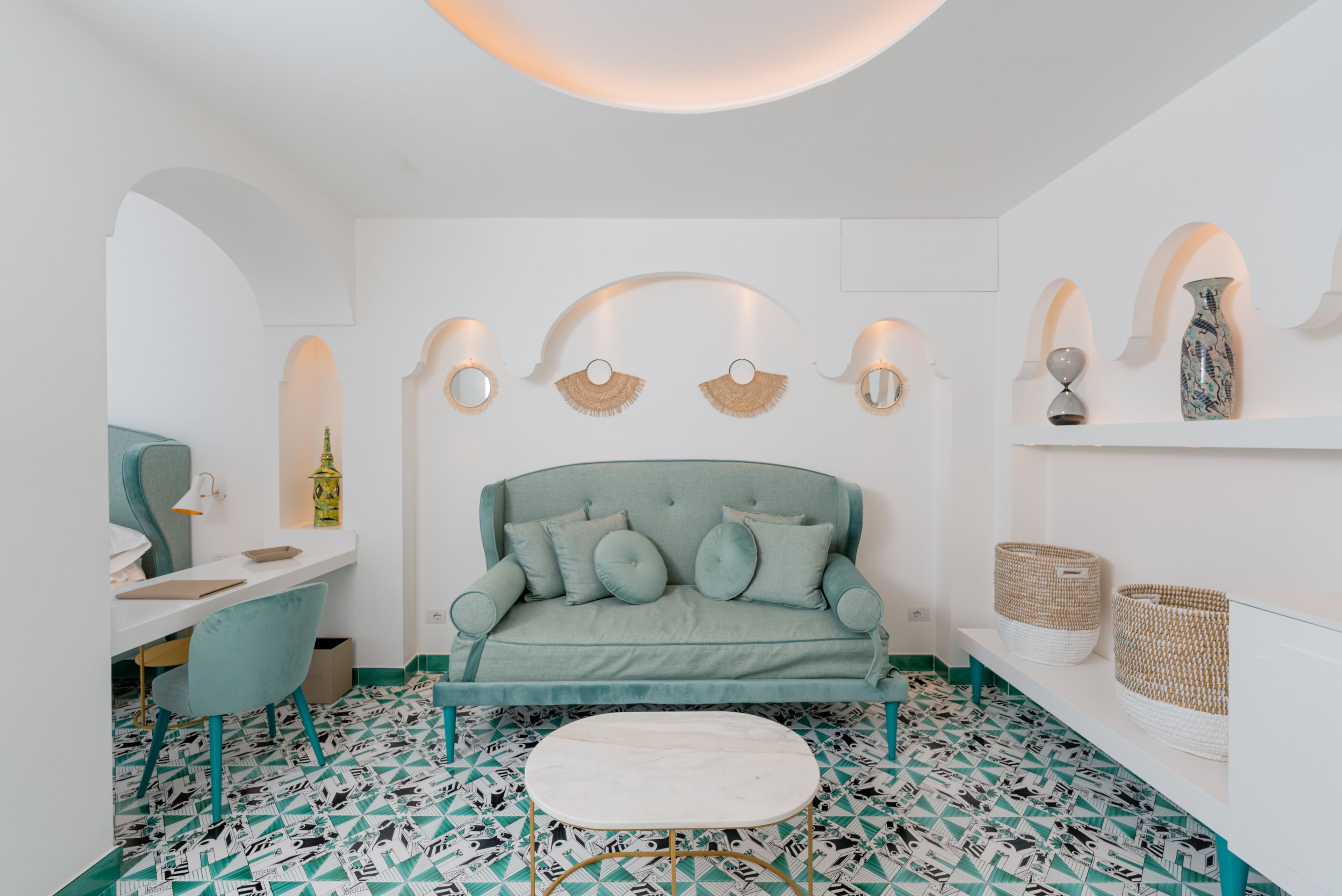 A modern room with a teal sofa, a white coffee table, and patterned flooring.