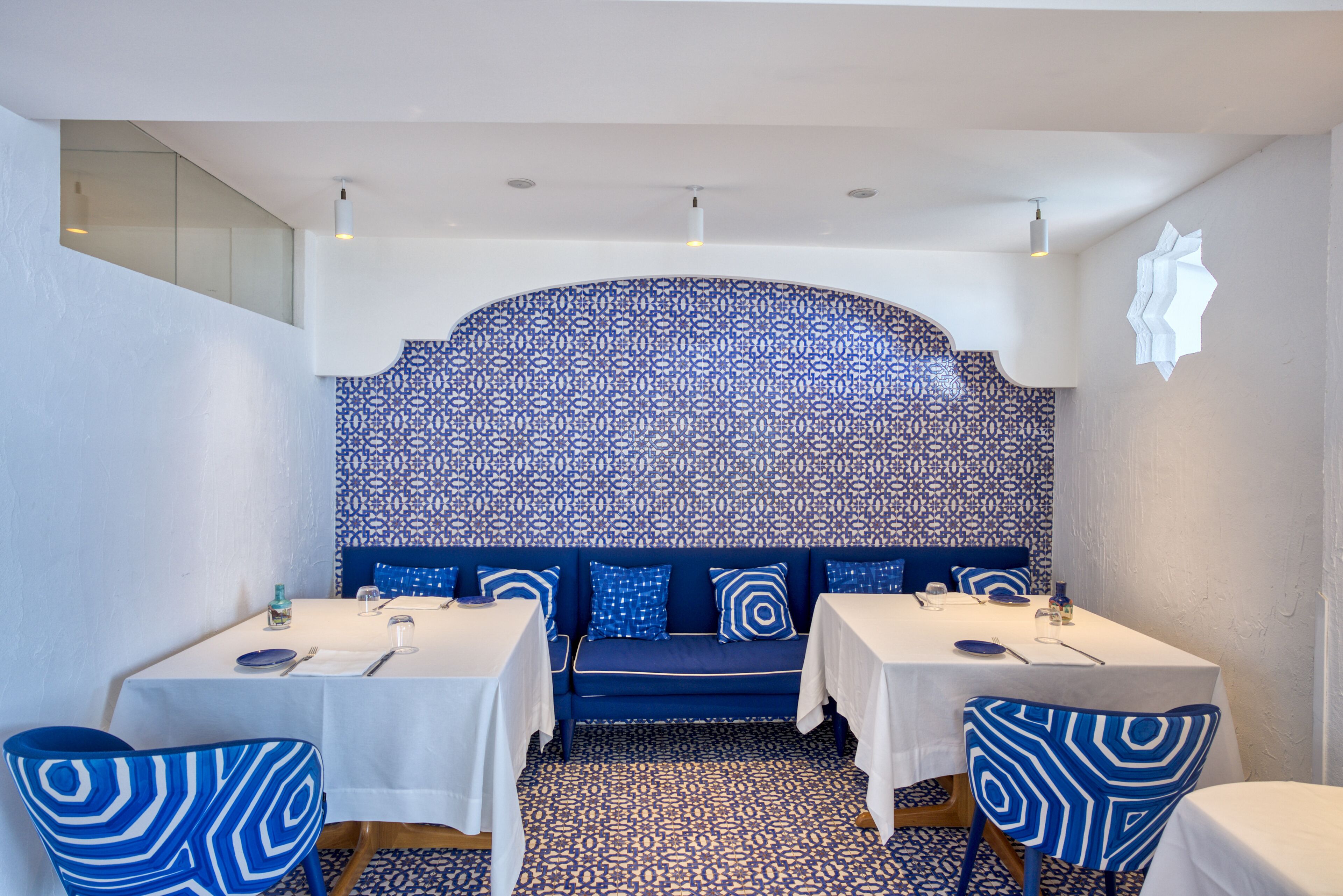 Un coin repas avec deux tables, un mur orné d’un motif bleu et un canapé bleu.