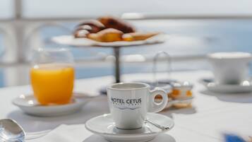 A breakfast setup with a coffee cup labeled "HOTEL CETUS" on a table, a glass of orange juice, and a plate of croissants.