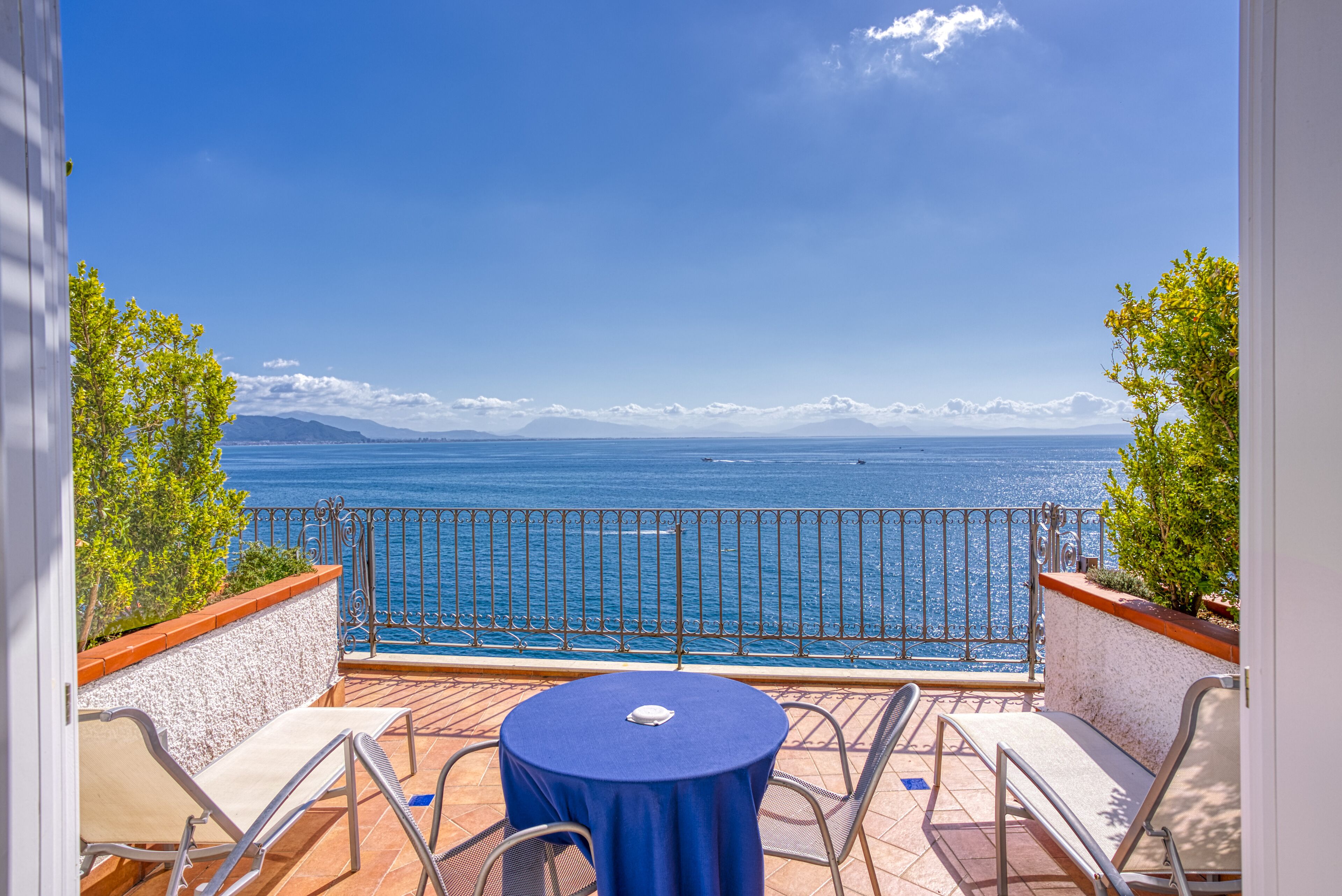 A balcony with a table and chairs, overlooking a body of water and distant mountains.
