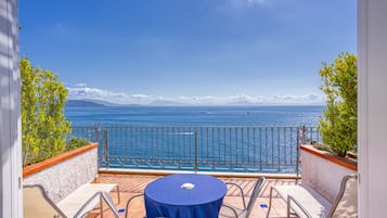 A balcony with a table and chairs, overlooking a body of water and distant mountains.