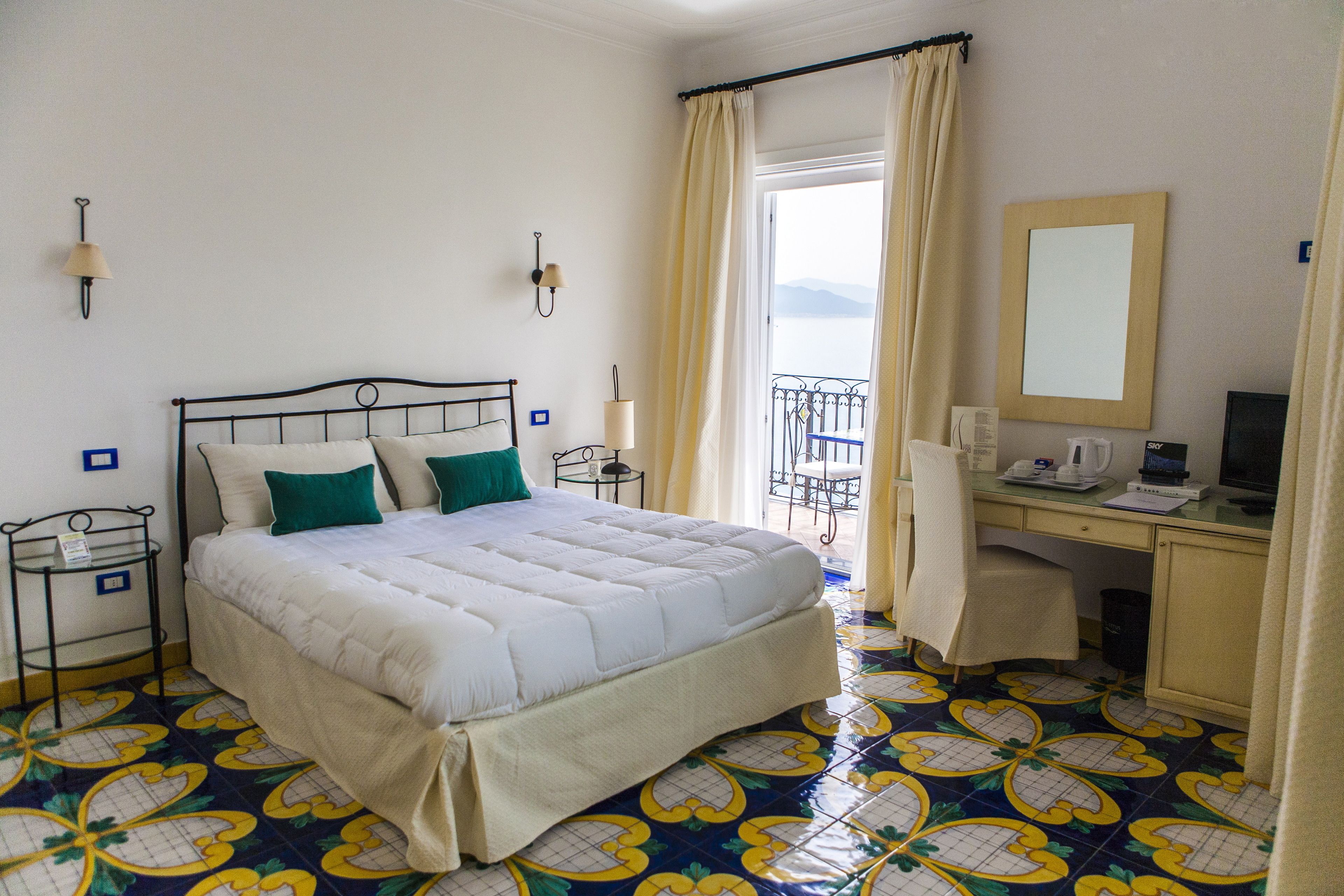 Habitación de hotel con cama, escritorio, silla, computadora y ventana con cortinas.