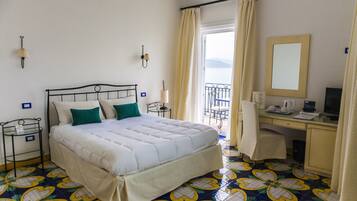 Habitación de hotel con cama, escritorio, silla, computadora y ventana con cortinas.
