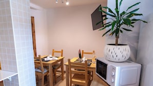 Cocina compacta con microondas, mesa de comedor de madera, sillas y una planta en maceta.