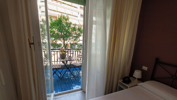 Habitación de hotel con cama, mesita de noche, lámpara y vistas a una piscina exterior y un balcón.