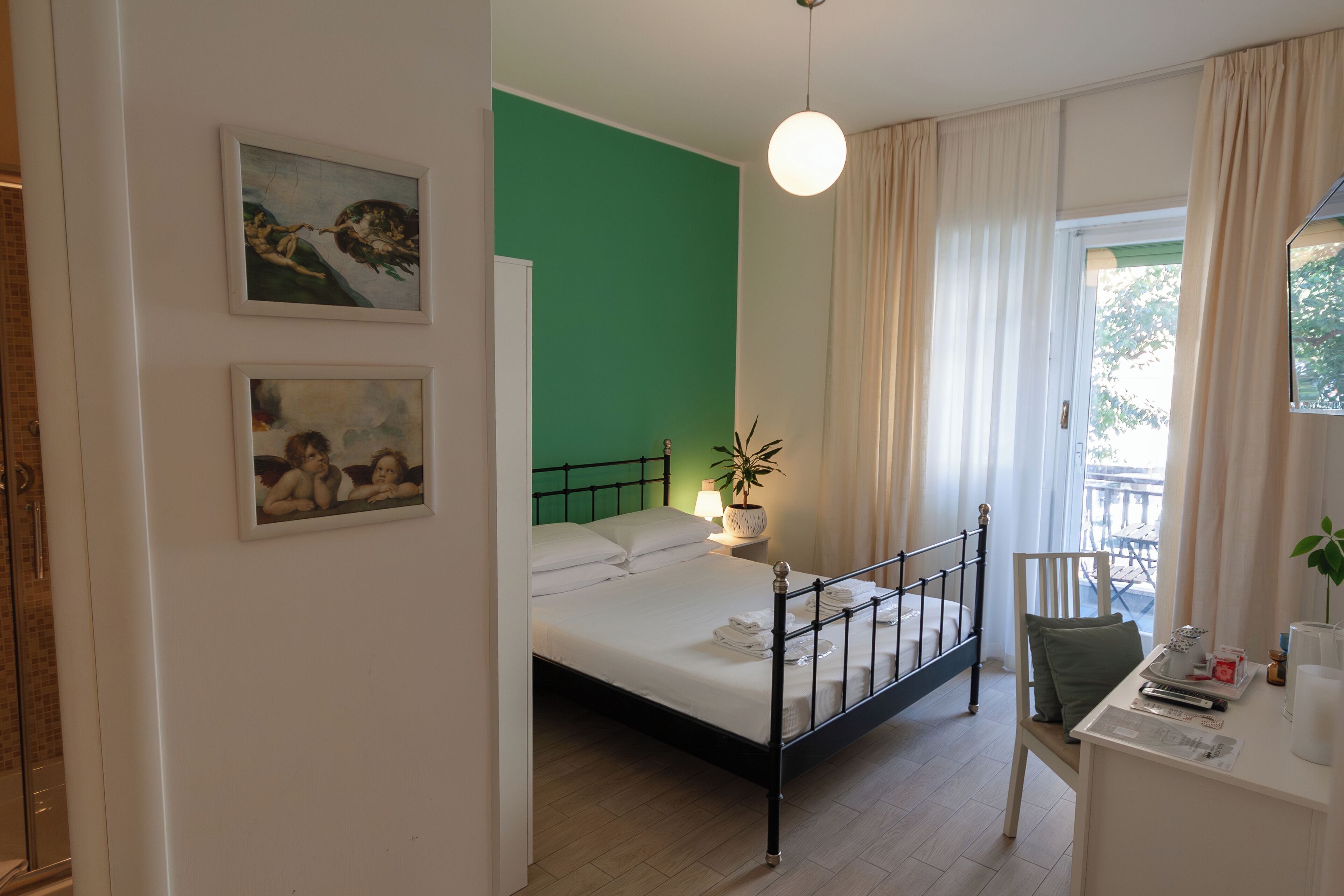 Un dormitorio con cama, escritorio, silla, planta en maceta y dos cuadros en la pared.