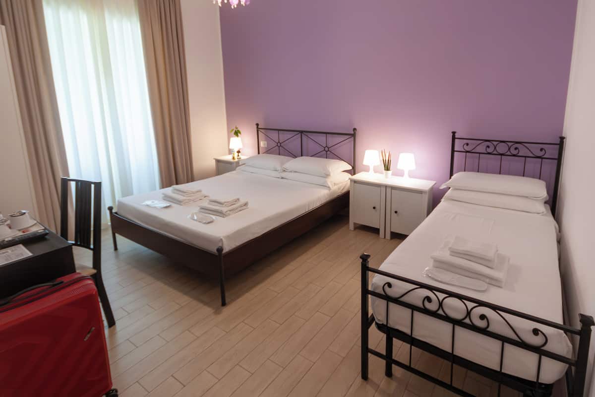 A hotel room with two beds, a desk, a chair, and a red suitcase.