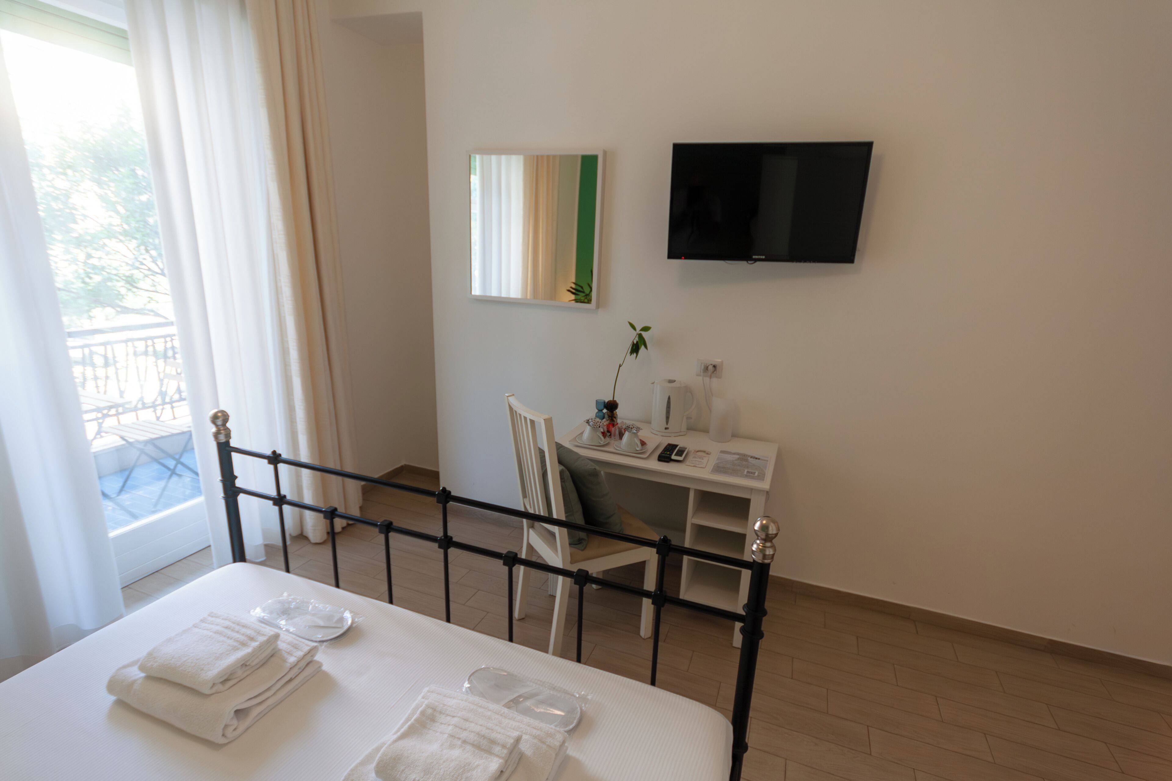 Quarto de hotel com cama, escrivaninha, cadeira, televisão e janela com cortinas.