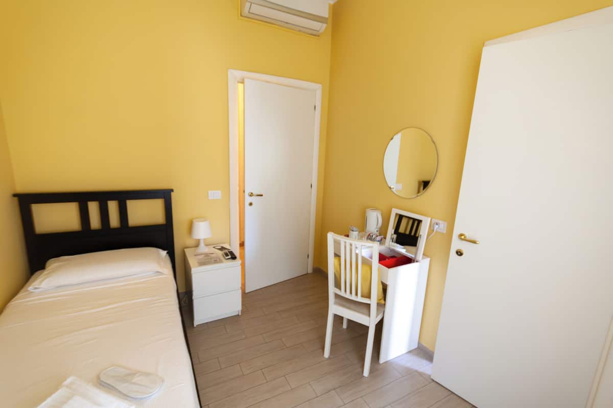 A room with a bed, a desk with a chair, a mirror, and a door.