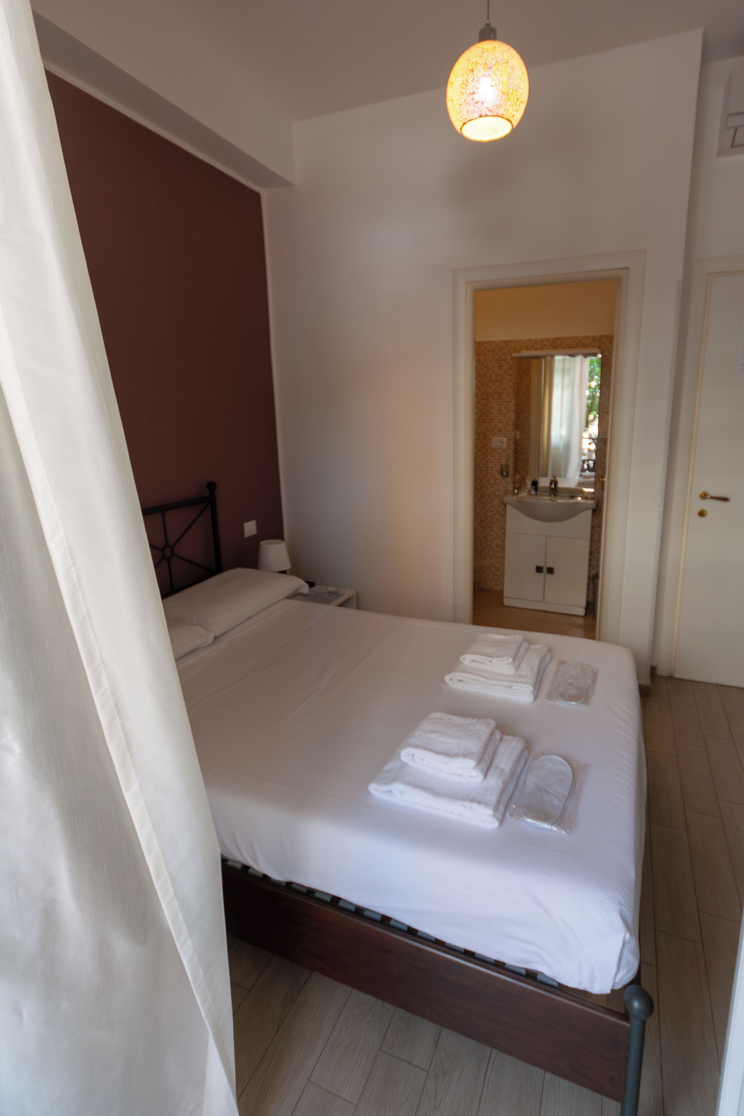 A neatly made bed with white linens and towels, a bedside lamp, and a door leading to a bathroom with a sink and mirror.