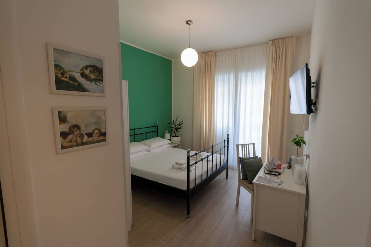 A bedroom with a bed, a desk, a chair, a TV, and two paintings on the wall.