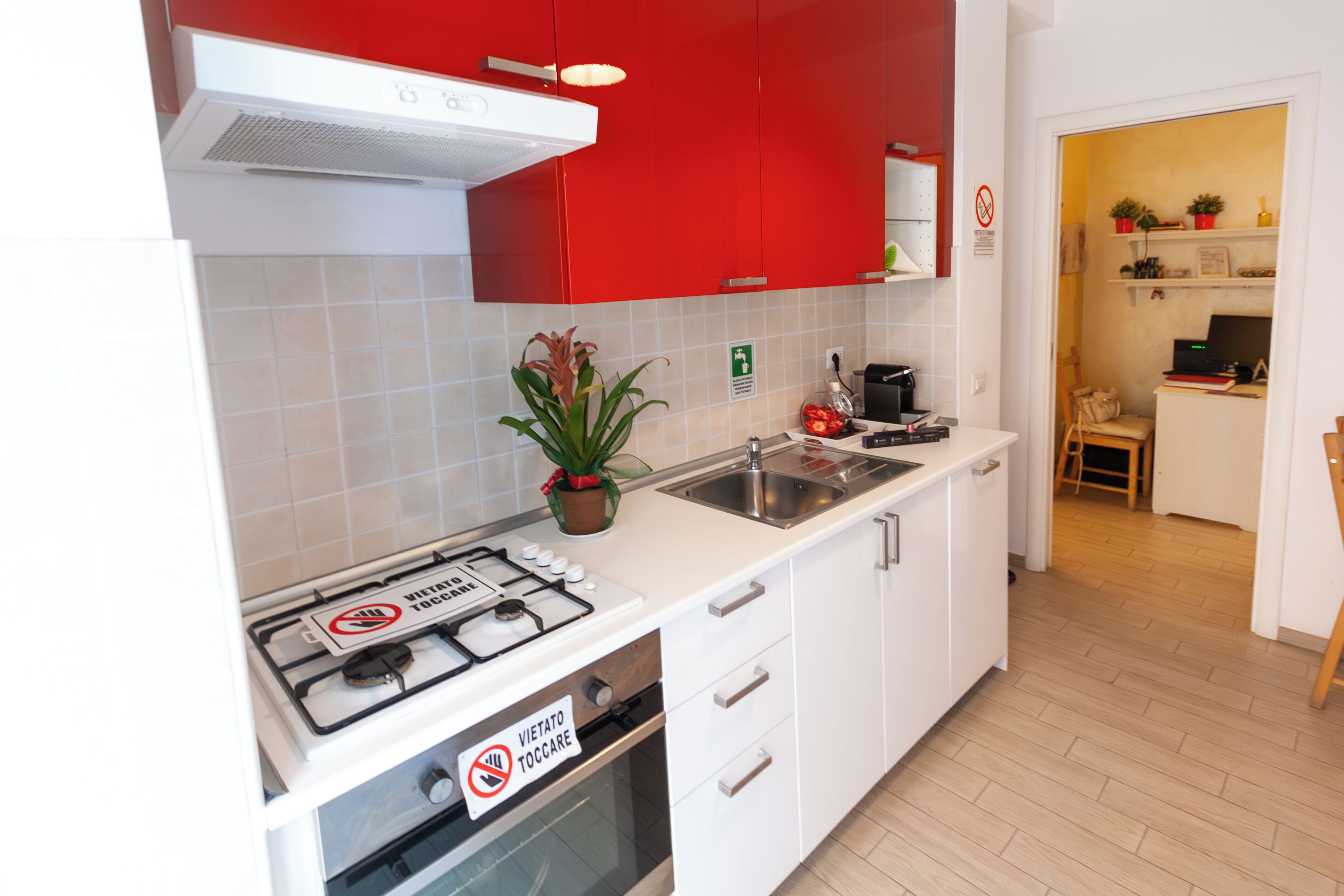 Une cuisine avec des meubles blancs, une partie supérieure rouge, une cuisinière à gaz et un évier.