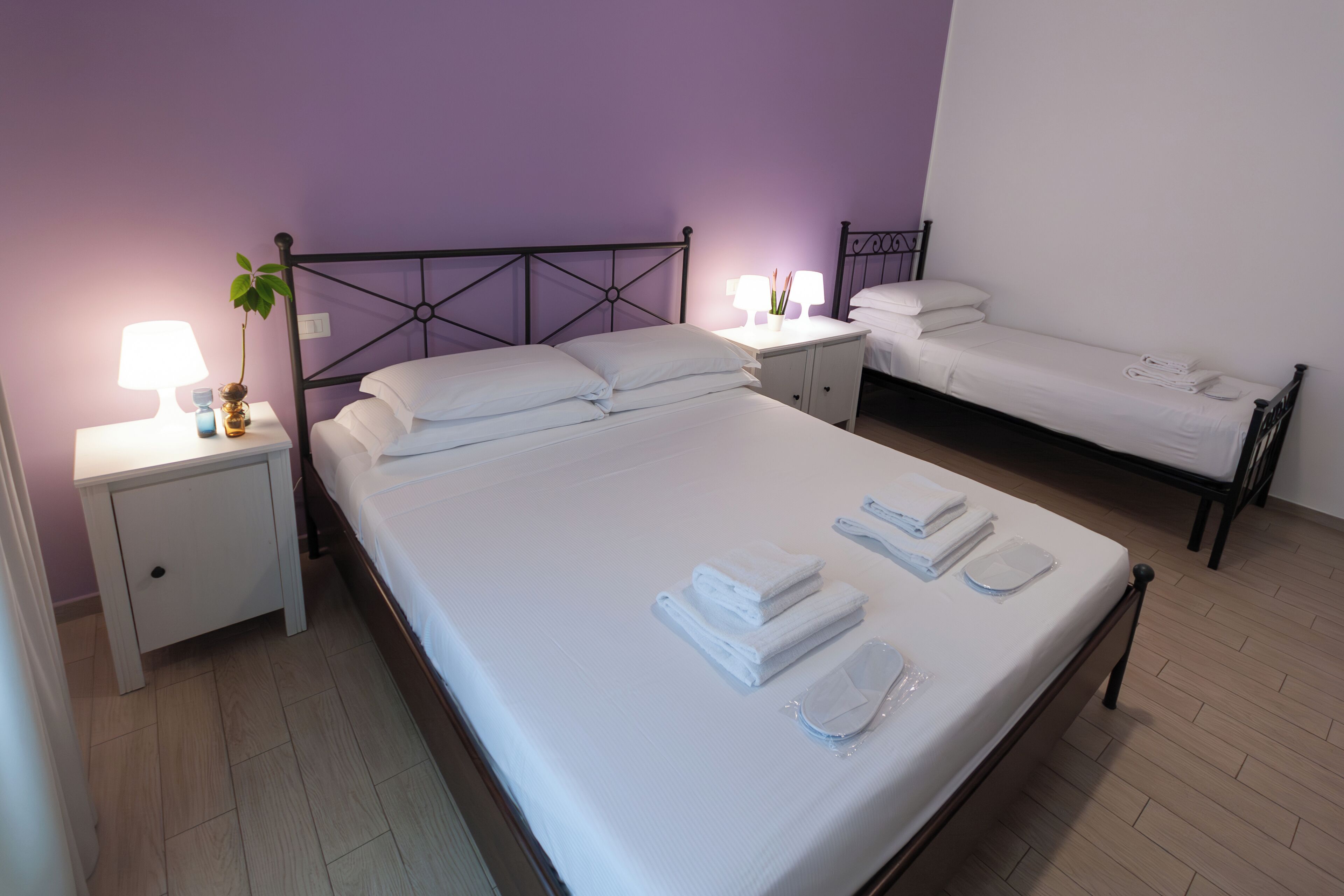 A hotel room with two beds, white linens, a nightstand with a lamp, and a potted plant.