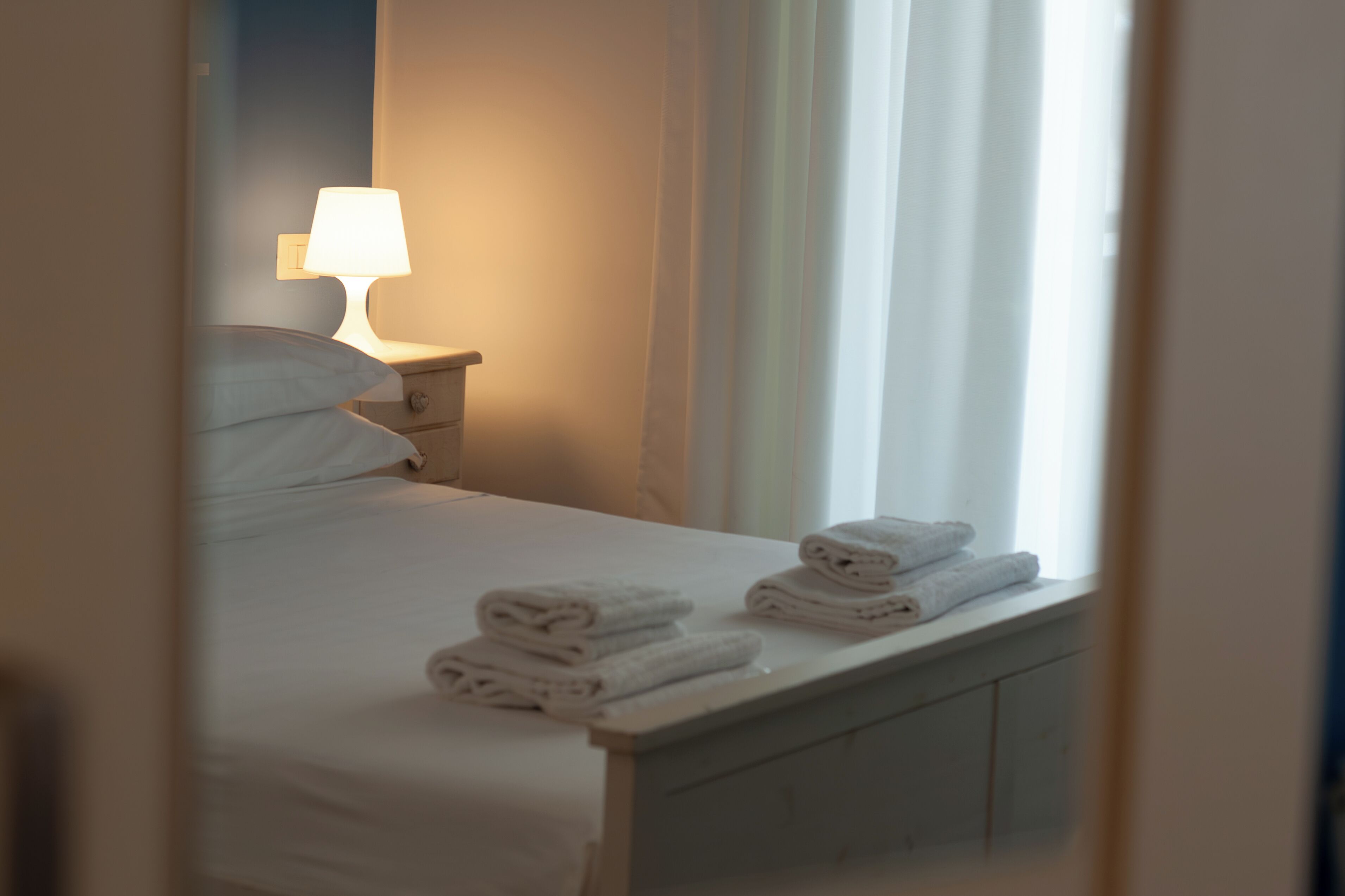 A hotel room with a neatly made bed, a bedside lamp, and a window with curtains.