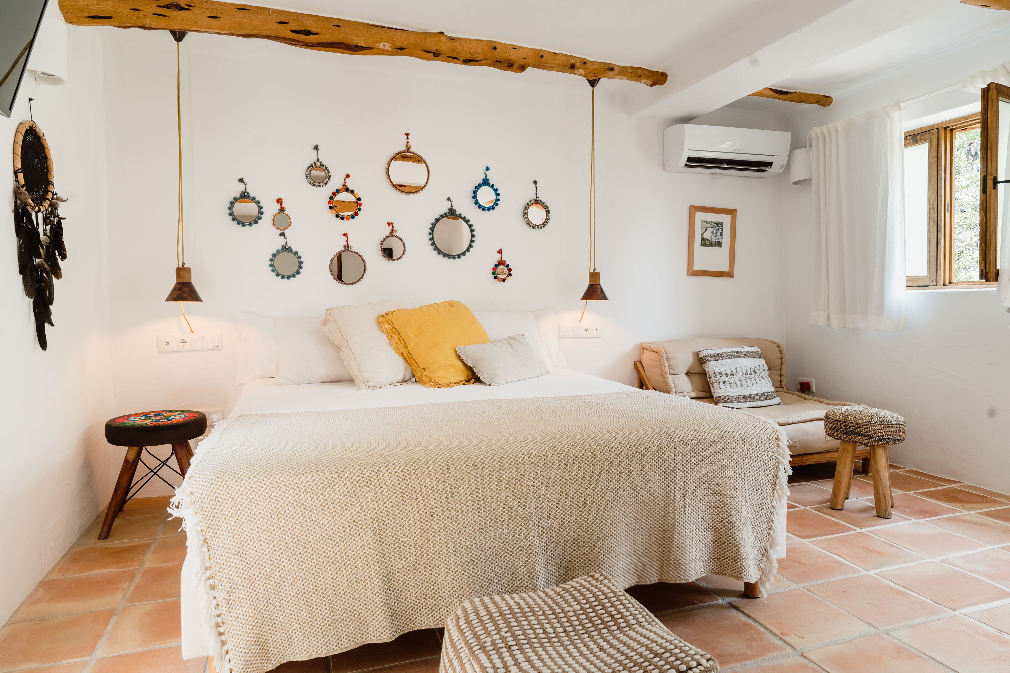 Un dormitorio con una cama grande, una mesita de noche, un taburete pequeño, una lámpara colgante y un aire acondicionado instalado en la pared.