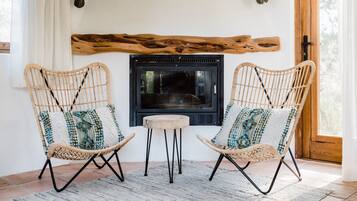 Two wicker chairs with cushions, a small round table, and a fireplace with a wooden beam above it.