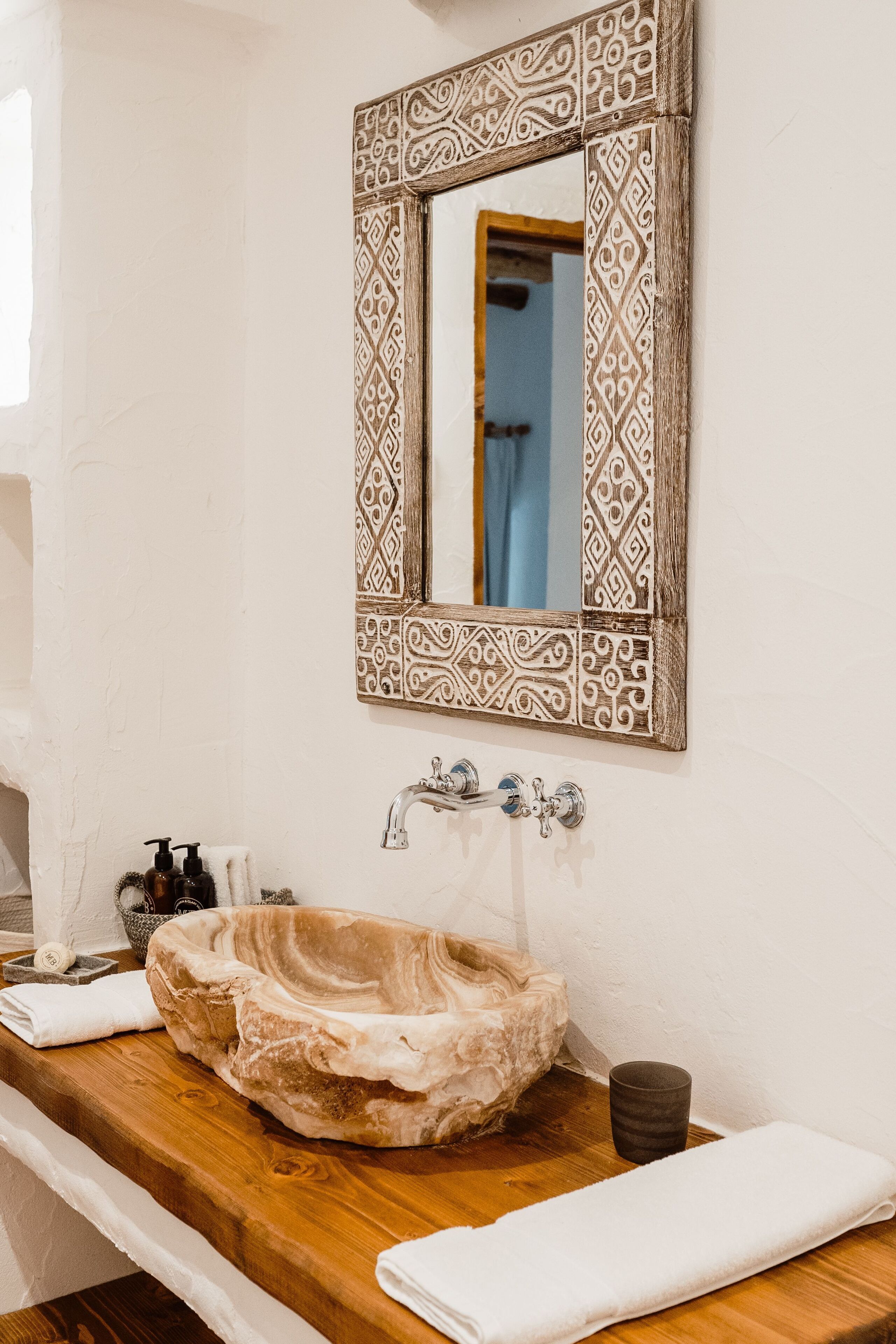 Un baño con lavabo de mármol, tocador de madera, marco decorativo para espejo y una toalla sobre la encimera.