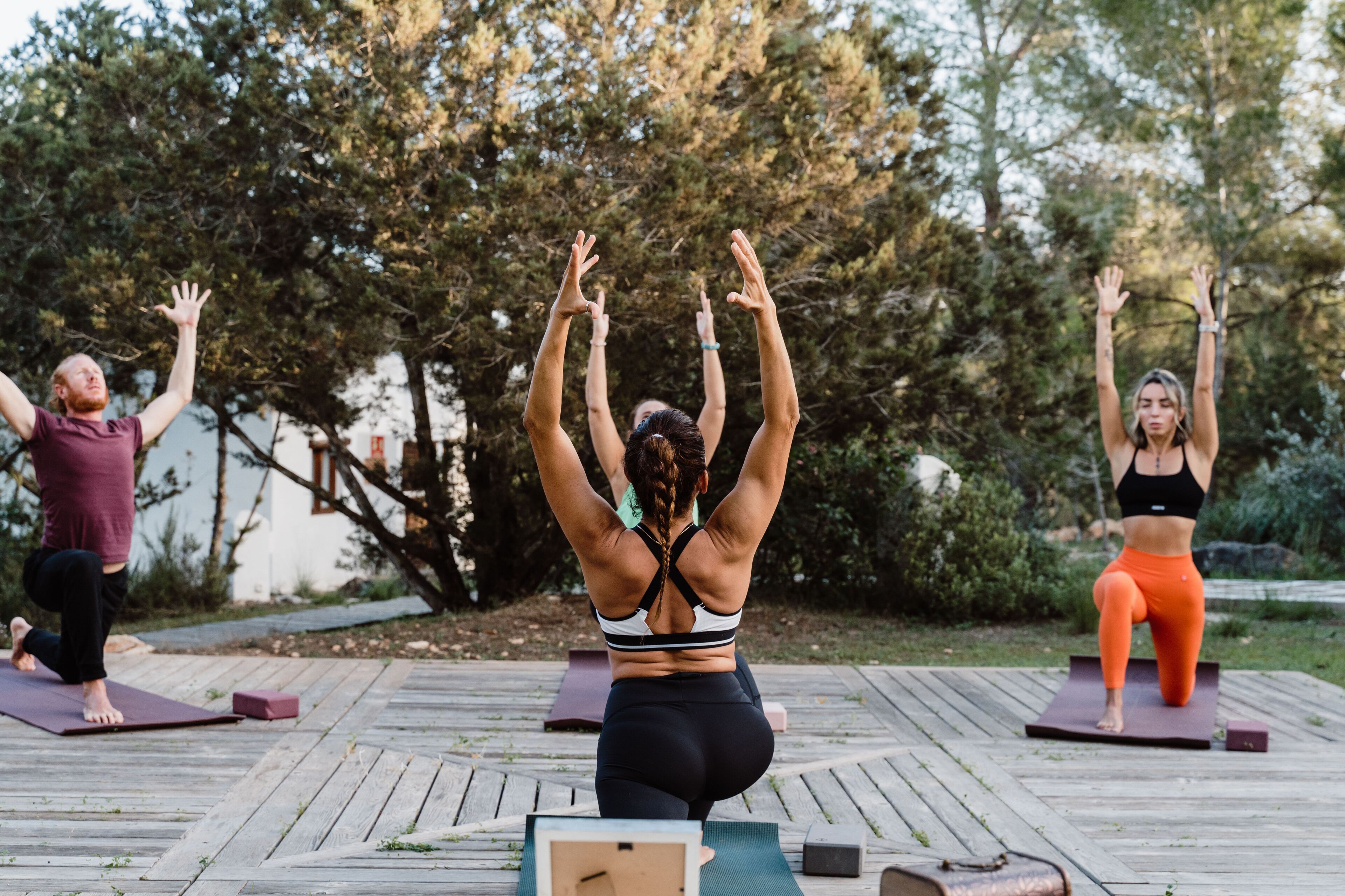 Tres personas practicando yoga sobre colchonetas en un área de maderas con árboles al fondo.