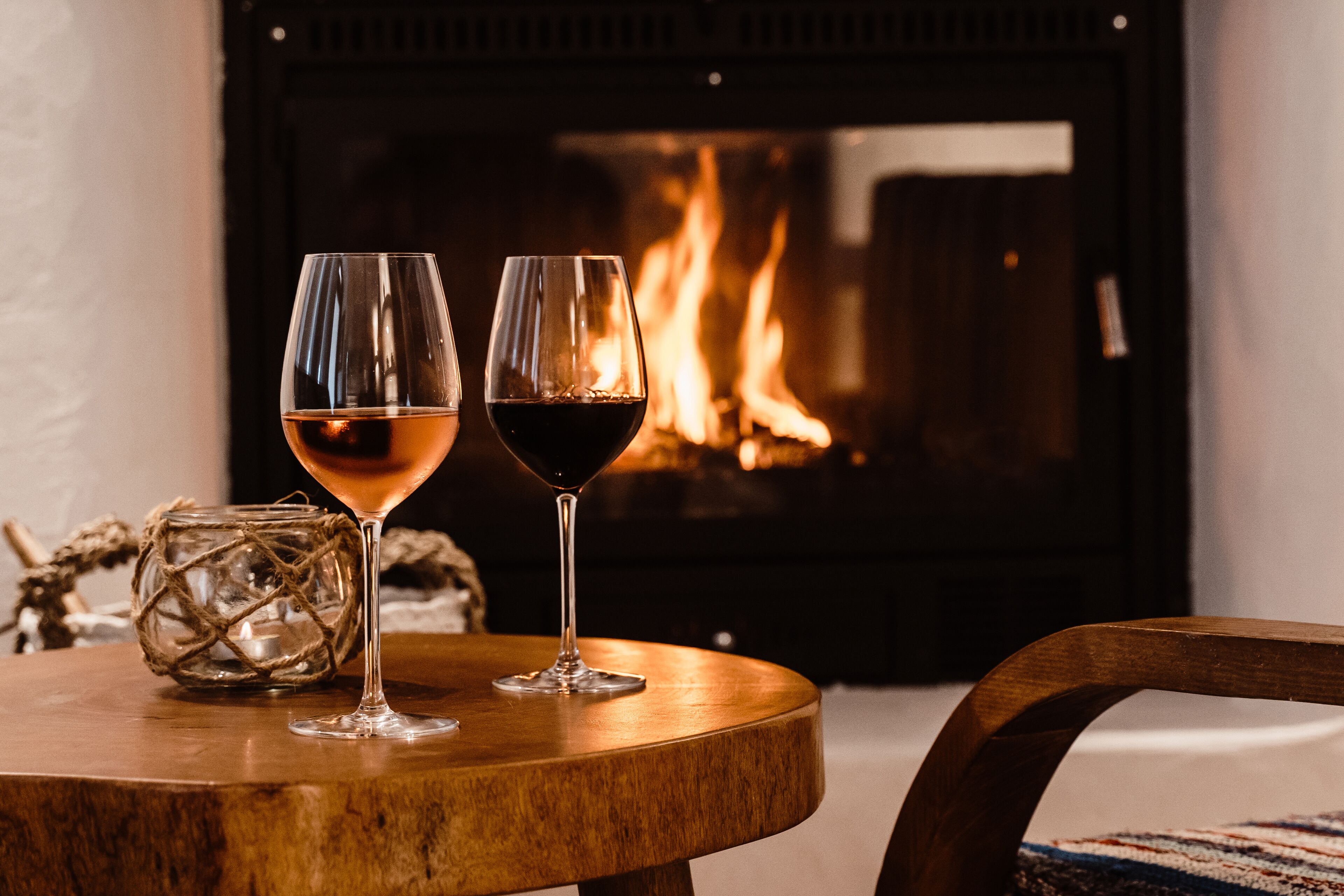 Dos copas de vino sobre una mesa de madera, con una chimenea al fondo.