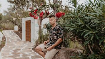 A man sitting on a rock by a stone pathway in a garden with red flowers and green foliage.