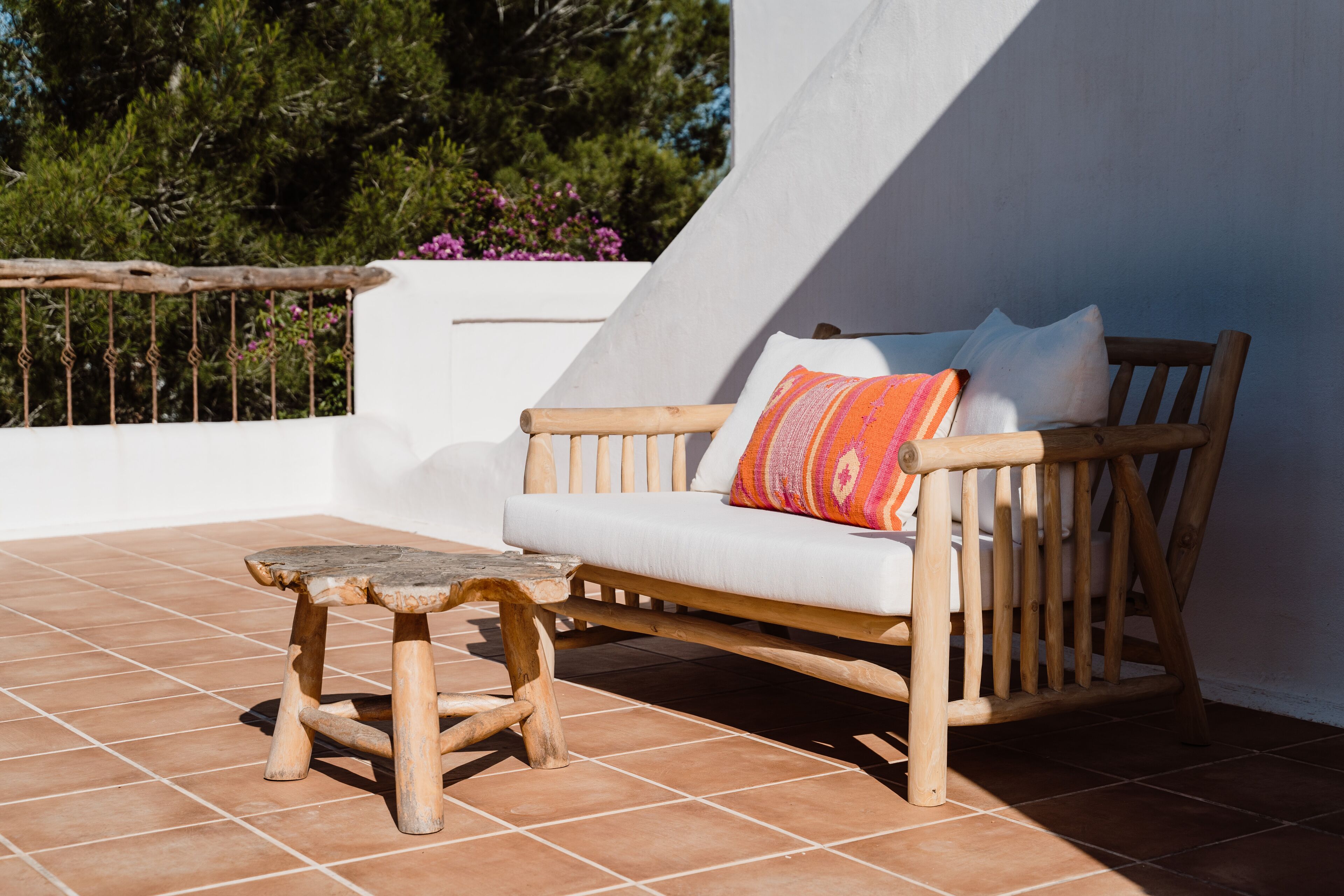 Un banc en bois et un canapé avec des coussins sur une terrasse carrelée.