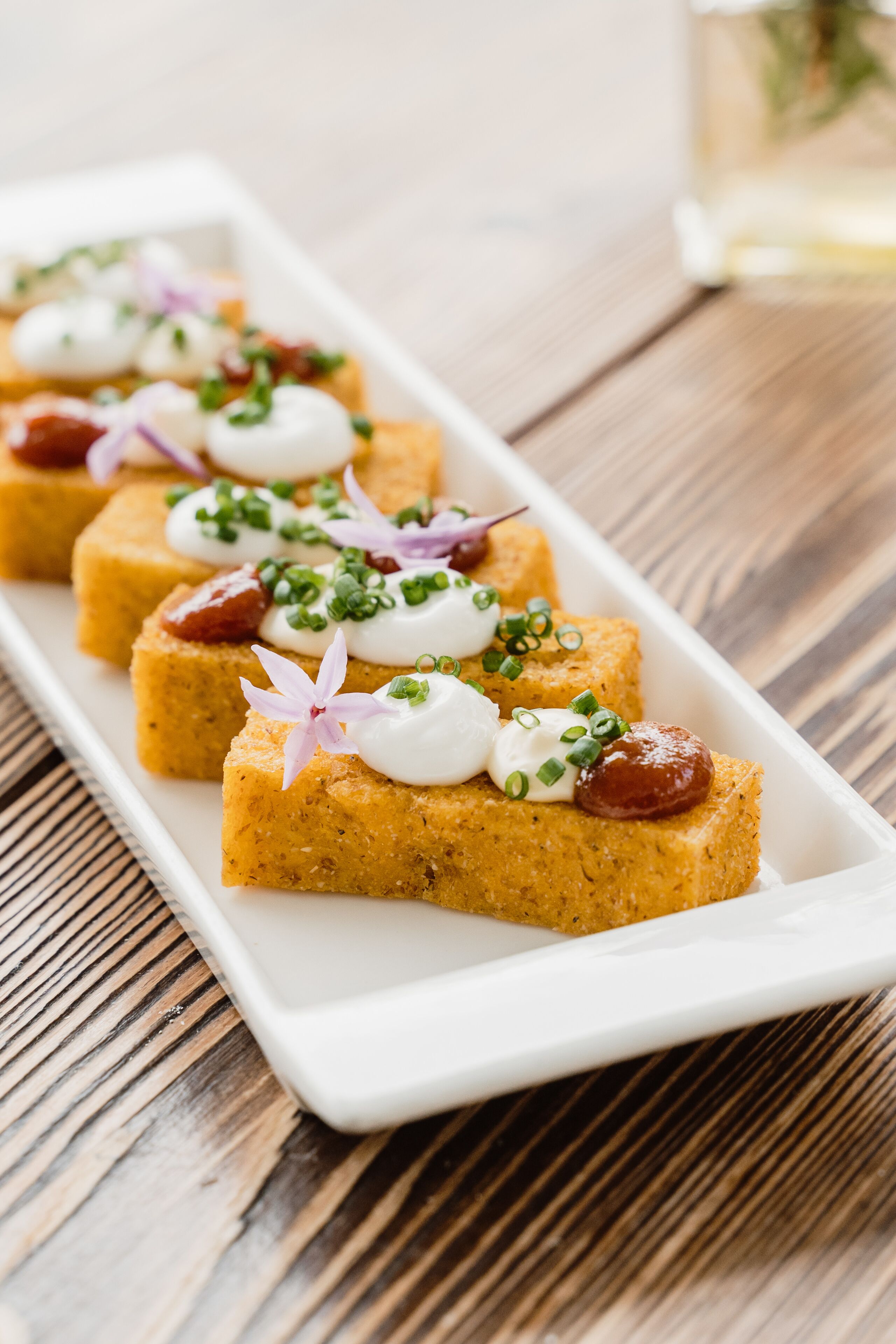 A white rectangular plate with several square pieces of food, garnished with green onions and a flower.