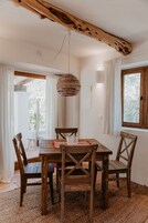 Un comedor con mesa y sillas de madera, una lámpara colgante de fibras tejidas y vistas al exterior a través de una ventana.