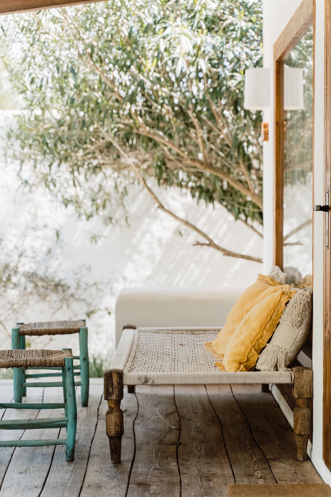 A wooden deck with a wicker sofa and a chair, a wooden table, and a view of trees through a glass door.