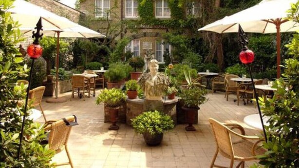 An outdoor patio area with tables and chairs, surrounded by potted plants and umbrellas. - Hotel Botticelli (Maastricht)