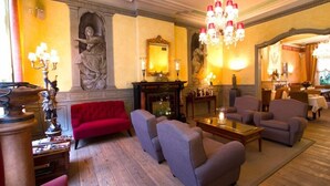 A room with a red sofa, grey armchairs, a chandelier, a fireplace, and a statue. - Hotel Botticelli (Maastricht)