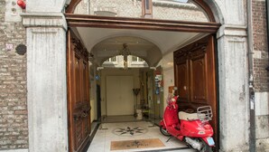 A red scooter parked at the entrance of a building with a tiled floor and a doormat. - Hotel Botticelli (Maastricht)