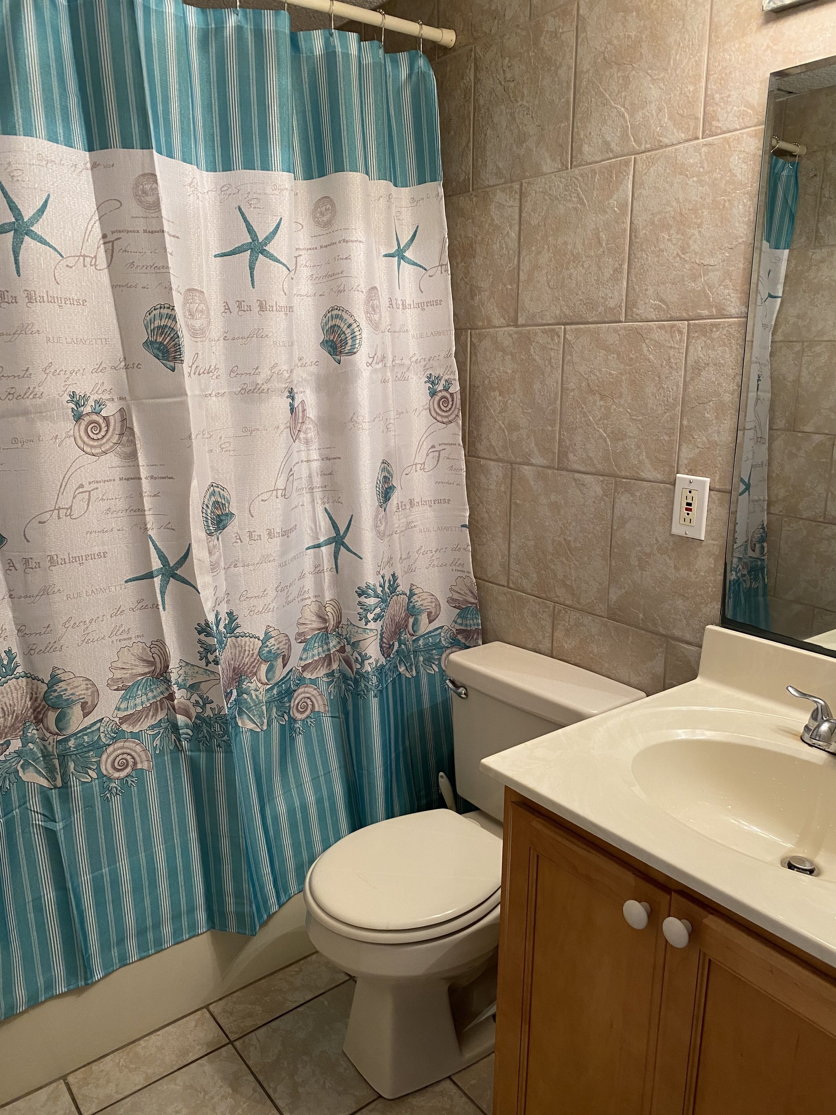 Un baño con cortina de ducha a rayas, un inodoro y un lavabo con armarios de madera.