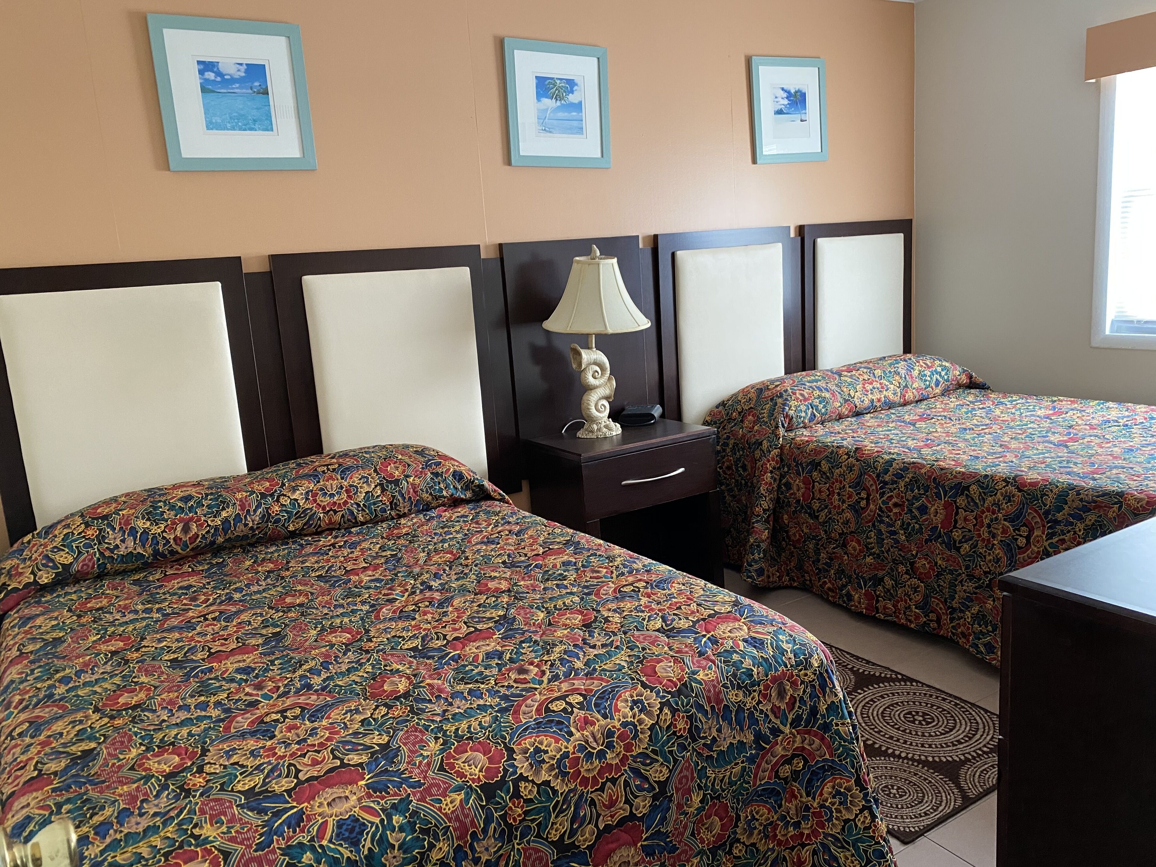 Una habitación de hotel con dos camas, una mesita de noche con lámpara y cuadros en la pared.