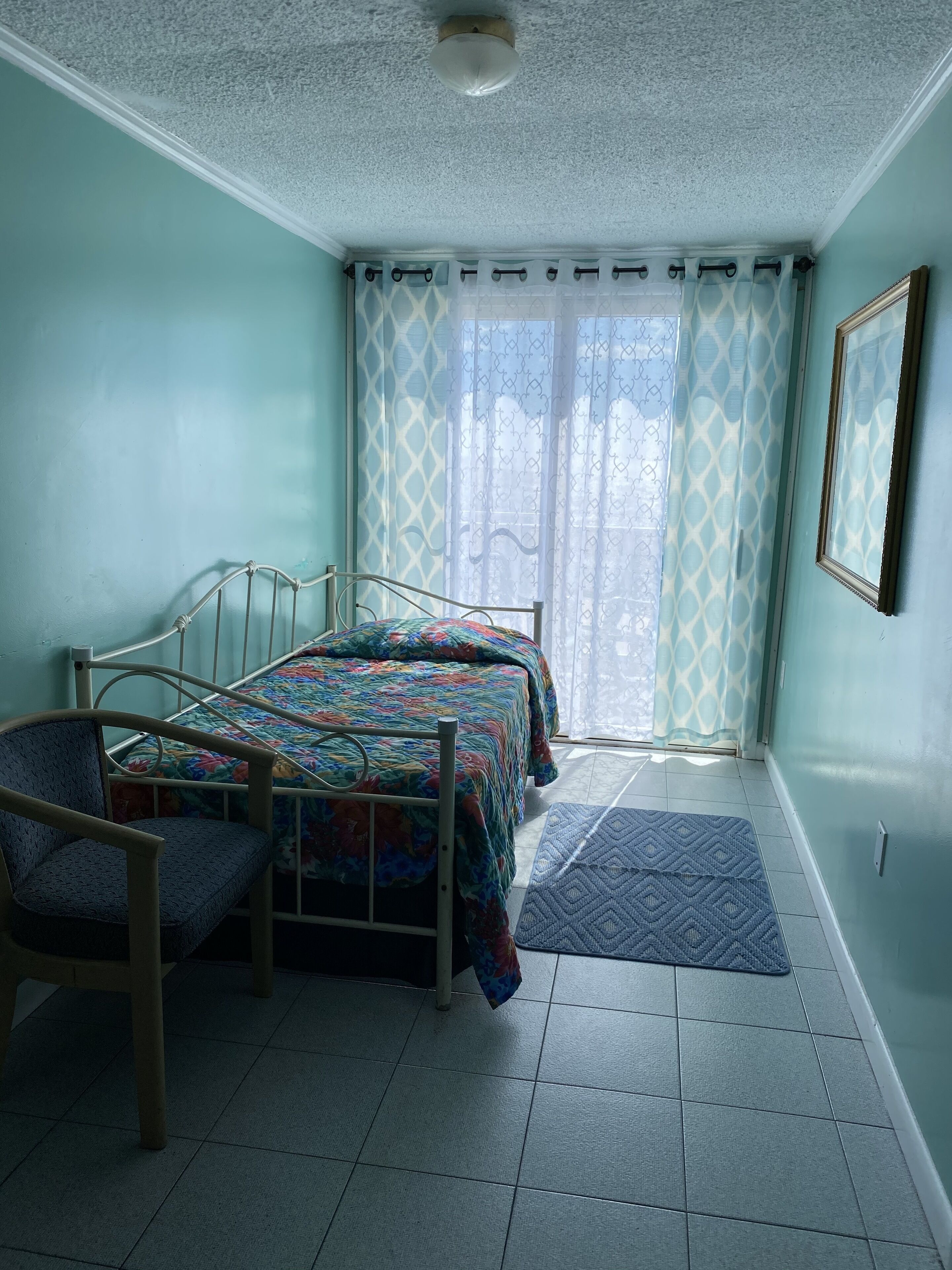 A bedroom with a bed, chair, and a window with curtains.