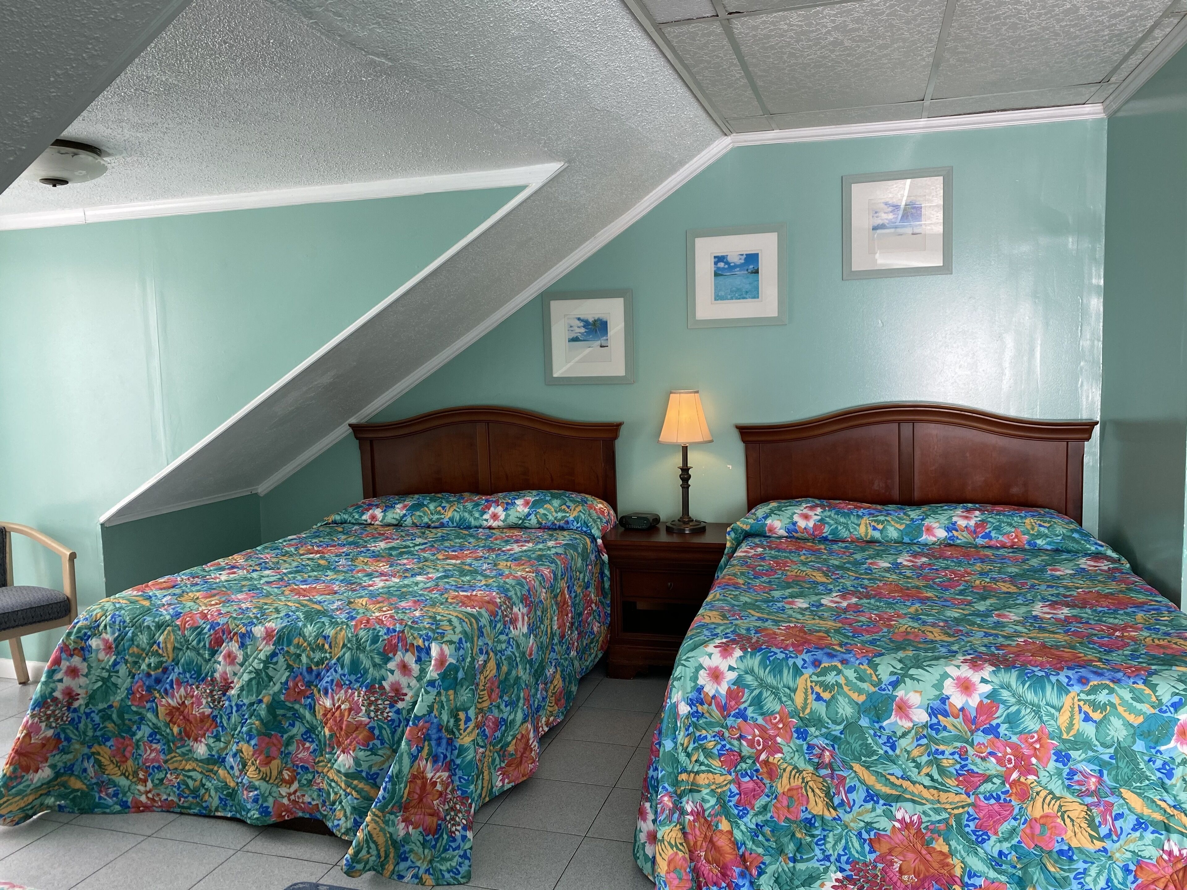 A room with two beds, each with a floral bedspread, a nightstand with a lamp, and a ceiling with a textured finish.