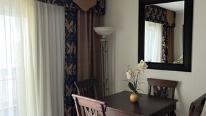 Un comedor con mesa de madera oscura, dos sillas, un florero con flores y un espejo en la pared.