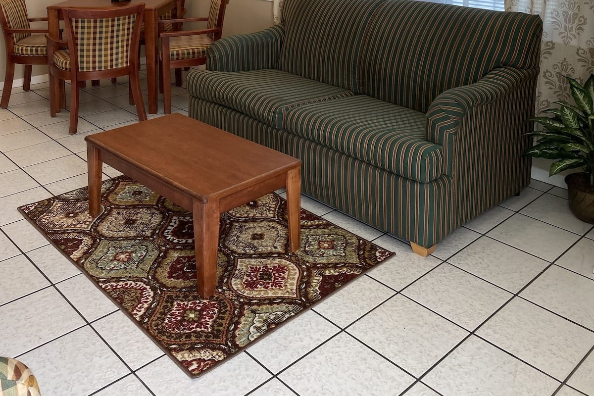 Ein Wohnzimmer mit einer Couch, Sesseln, einem Couchtisch, einem Teppich, einem Spiegel und einem Fenster mit Vorhängen.