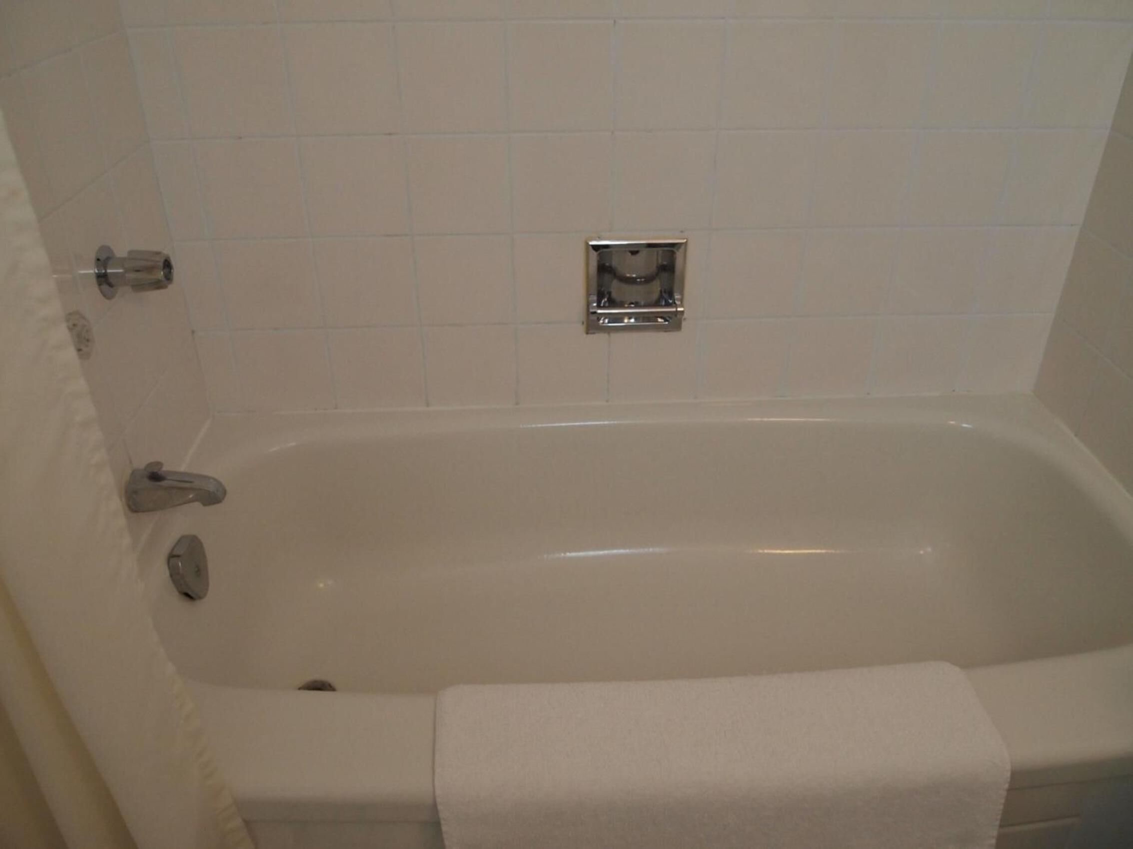A standard white bathtub with a chrome faucet and a small control panel on the wall.