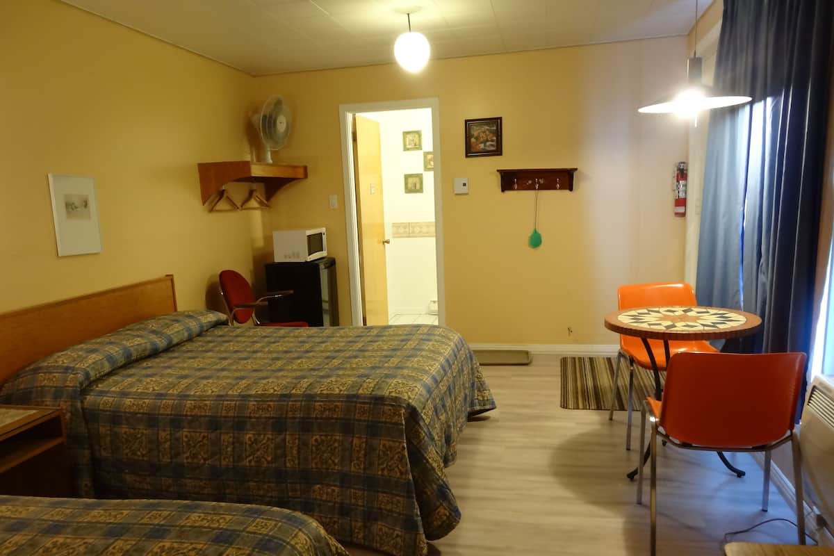A room with two beds, a small table with chairs, a microwave, and a door leading to another room.