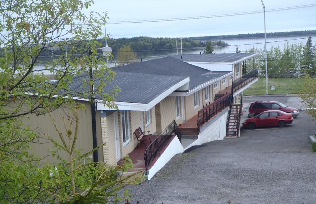 Un motel con un área de estar cubierta al aire libre, una escalera que conduce a un segundo piso y un estacionamiento con dos coches.