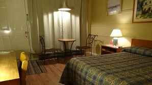 Een hotelkamer met een bed, een bureau, een stoel, een klein tafeltje, een lamp en gordijnen.