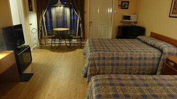 Habitación de hotel con dos camas, televisión, una pequeña mesa con sillas y puerta que da a un balcón.