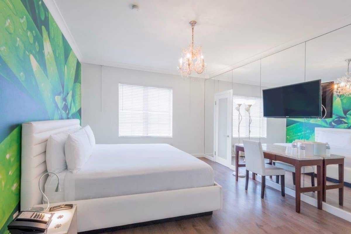 A hotel room with a large bed, a desk with a chair, a television, and a chandelier.