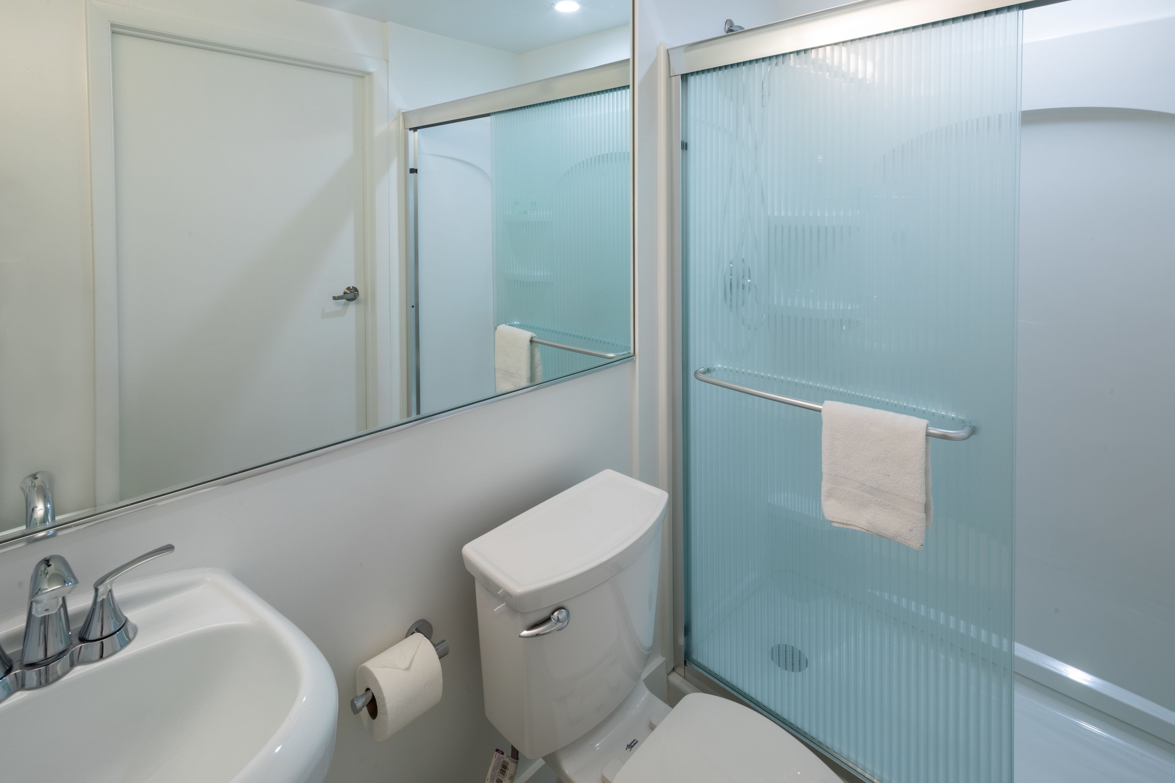 A bathroom with a white sink, toilet, and glass shower enclosure.