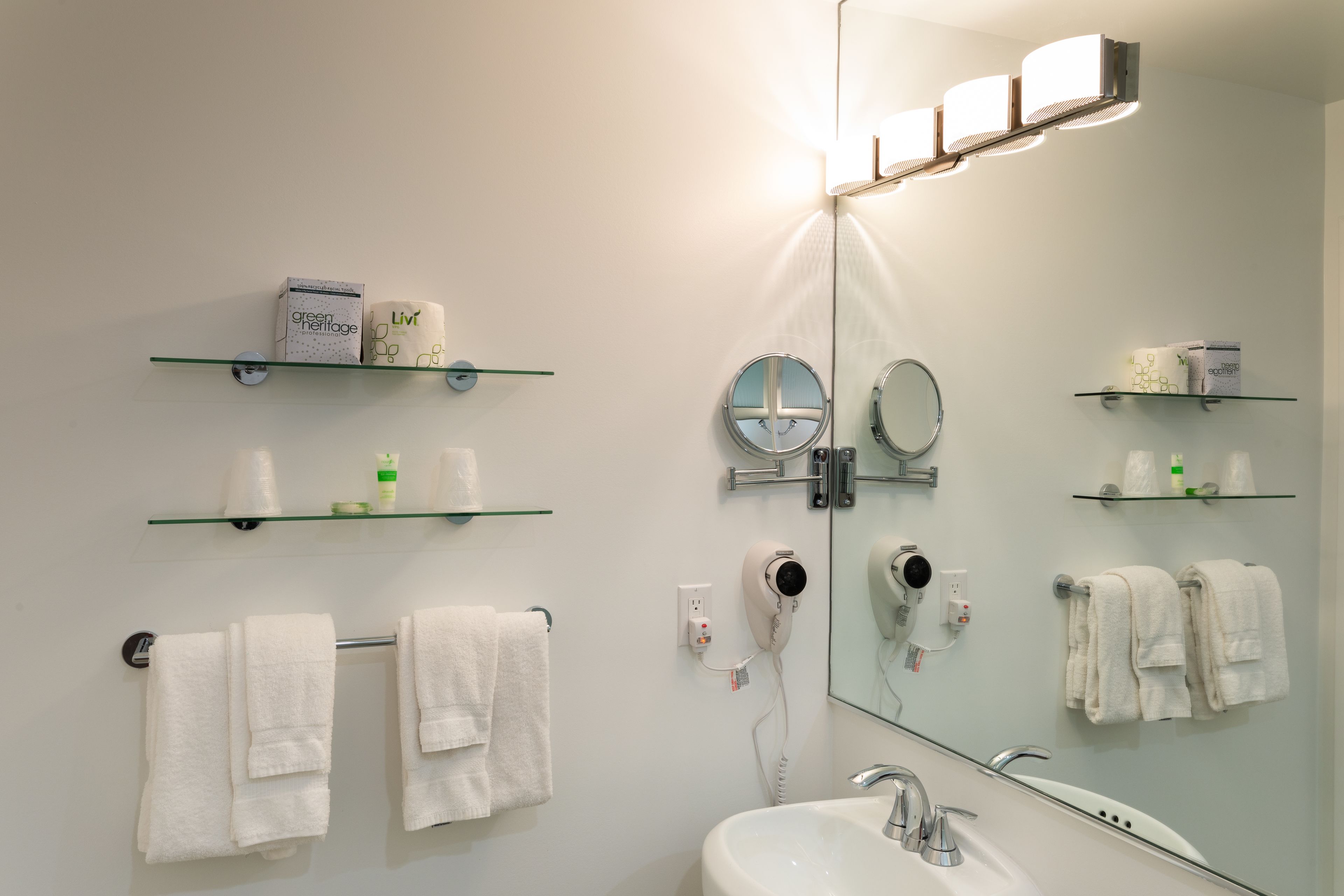 A bathroom with a sink, mirror, and towel rack. There are shelves with toiletries and a hairdryer.