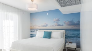 Une chambre avec un grand lit, une table de chevet, une fresque murale représentant l’océan et une grille d’aération au plafond.