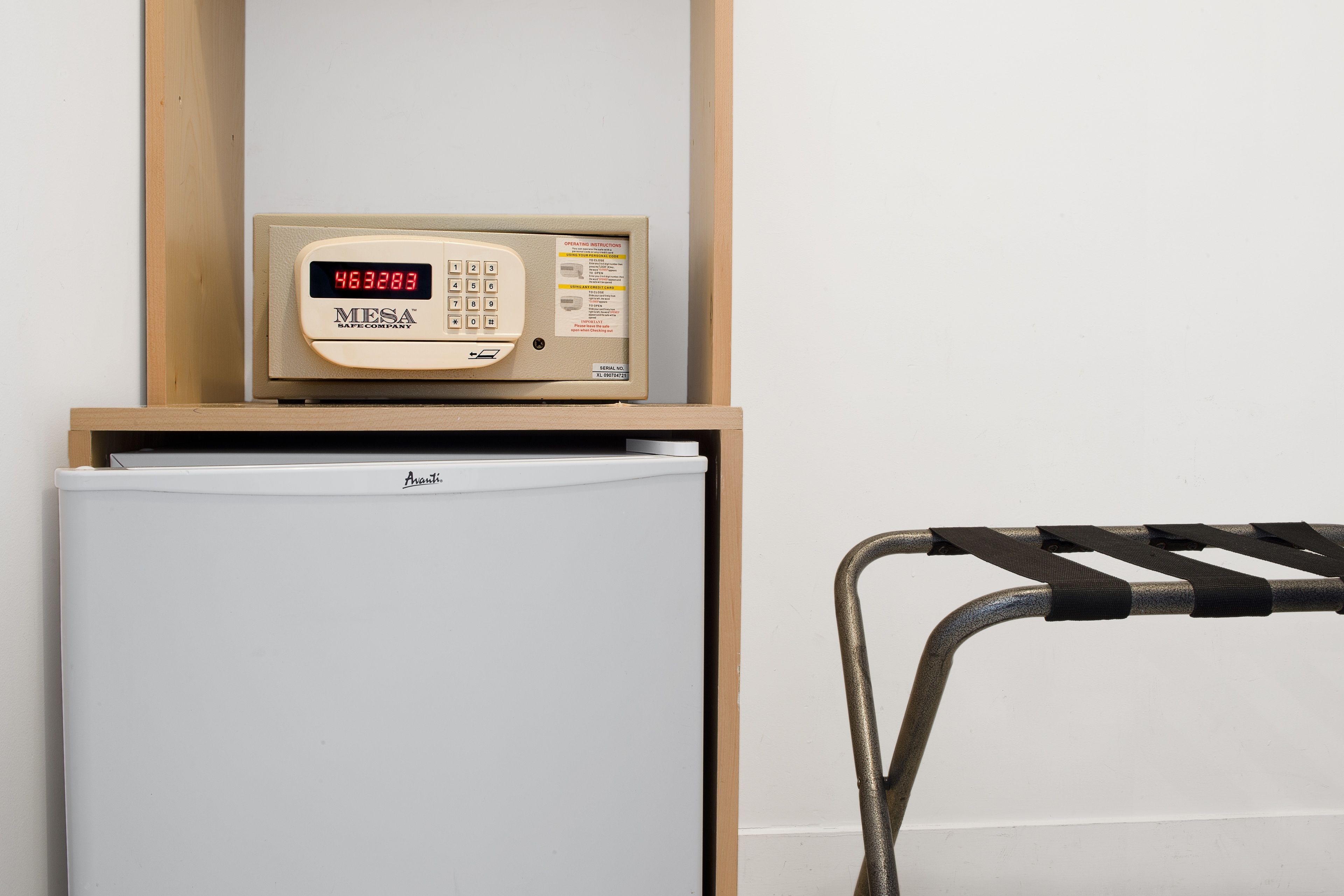 A compact refrigerator with a digital display, a microwave on top, and a chair with a metal frame.