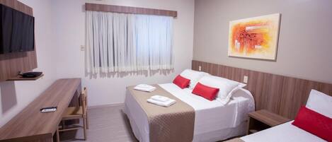 Una habitación de hotel con cama, mesitas de noche, escritorio, silla, aire acondicionado y un cuadro en la pared.