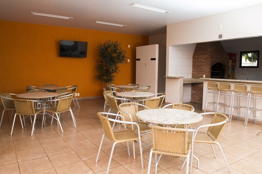 Un restaurante con mesas redondas y sillas de mimbre, un televisor montado en la pared y un horno de ladrillo.