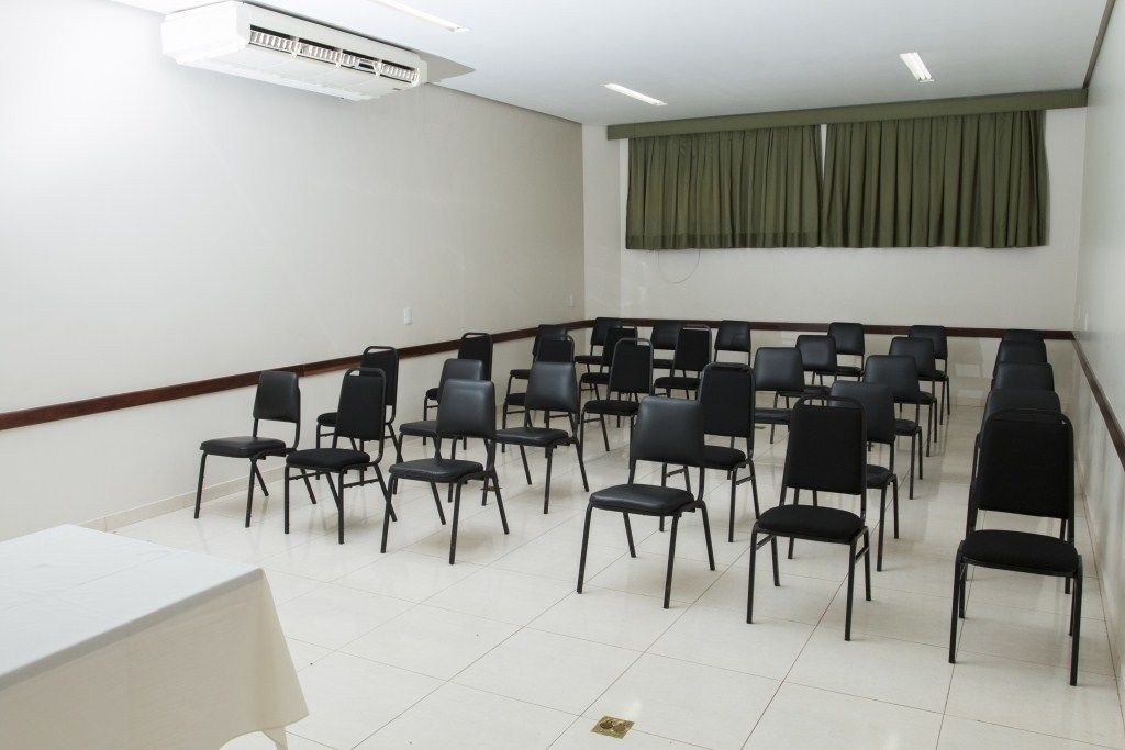 A conference room with rows of black chairs, a white table, and a large window with green curtains.
